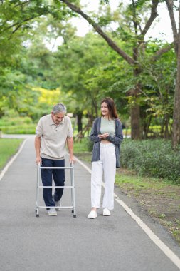 Yaşlı bir adam, genç yetişkin bir kızla parkta Walker Yardım Rehabilitasyonu 'nu kullanıyor.