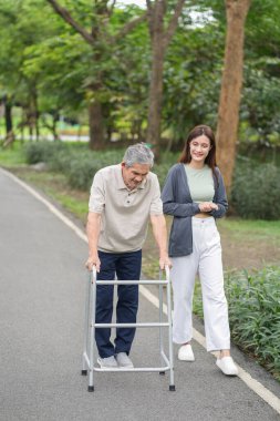 Yaşlı bir adam, genç yetişkin bir kızla parkta Walker Yardım Rehabilitasyonu 'nu kullanıyor.