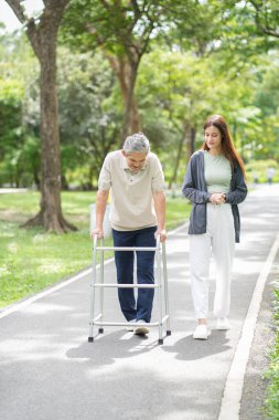 Yaşlı bir adam, genç yetişkin bir kızla parkta Walker Yardım Rehabilitasyonu 'nu kullanıyor.