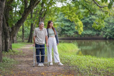 Yaşlı bir adam, genç yetişkin bir kızla parkta Walker Yardım Rehabilitasyonu 'nu kullanıyor.