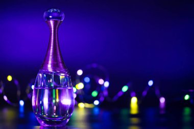 Siyah arka planda renkli ışıklarla aydınlatılmış bir şişe parfüm.