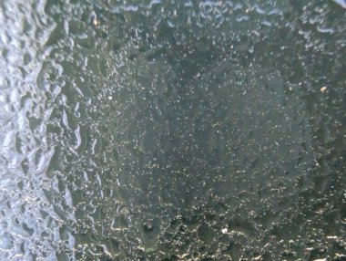 Sisli bir cam yüzeyde yağmur suyu damlacıkları dış dünyanın görüntüsünü bozuyor. Bu doğa olayı yağmurlu bir günde havanın ve ışığın güzelliğini yakalar..