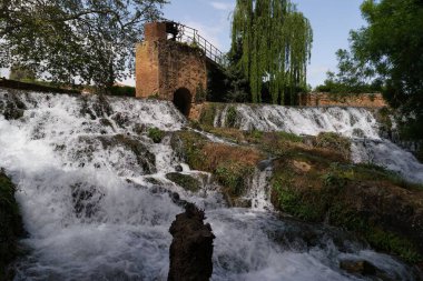 Antik bir su kemeri bölgesindeki bir dizi kayalık şelaleden akan sular. Uzun ağaçlar ve yeşillikler çağlayan suyun etrafını sarar ve sakin bir atmosfer yaratır..