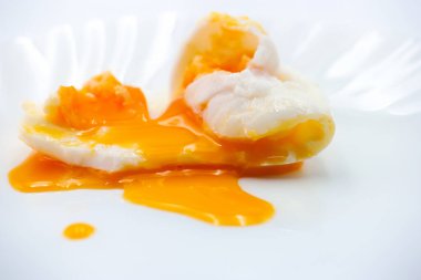 Haşlanmış bir yumurta temiz beyaz bir tabakta oturur, beyaz, dışarı sızan canlı sarı sarısını sarar. Sunum yumurtanın pürüzsüz dokusunu ve tazeliğini vurguluyor.