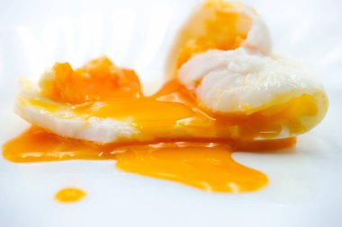 İki mükemmel haşlanmış yumurta, beyaz bir tabakta dinleniyor ve parlak turuncu sarılarının döküldüğünü gösteriyor. Bu yemek, kremalı klasik bir kahvaltı tercihi sunuyor..