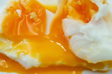 Canlı turuncu sarısı olan iki mükemmel haşlanmış yumurta beyaz bir tabakta, sıcak ve sulu sarıları dökülüyor. Bu kahvaltı yemeği güne çok lezzetli başlıyor..