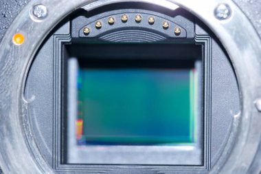 Yakın plan, mekanik parçalarla çevrili kamera sensörünü ortaya çıkarıyor. Renkleri ve ışıktan yansımaları gösteriyor. Bu fotoğraf teknolojisinin işçiliğini vurguluyor.