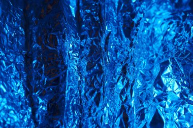 Parıldayan mavi metalik folyo yumuşak ışık altında kıvrımları ve yansımaları olan dokulu bir yüzey sergiler. Canlı renk, tüm görsel çekiciliği ve derinliği arttırır..