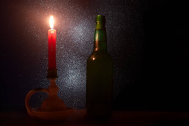 Kırmızı bir mum çevresini aydınlatır, yeşil bir şişenin yanında sıcak bir parıltı bırakır. Arkalarında, güzel yıldızlı bir gece gökyüzü huzurlu atmosferi güçlendirir..