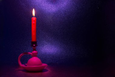 Kırmızı bir mum, parlak renklerin arkaplanına hafifçe ışık tutarak bir tutacakta sürekli yanar. Huzurlu ortam rahatlama veya meditasyon için uygun bir ortam yaratır..