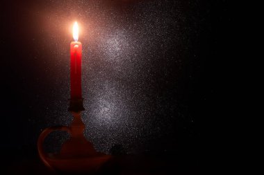 Karanlık bir ortamda tek bir kırmızı mum hafifçe yanar, ılık bir ışık saçarak havada süzülen parlak parçacıklarla sakin bir ortam yaratır, sakinlik ve nostalji uyandırır..