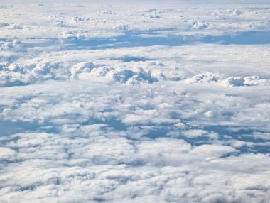 Kabarık beyaz bulutların geniş katmanları gökyüzünü dolduruyor, sakin bir mavi arkaplan üzerinde güzel bir manzara yaratıyor, açık gün ışığında çekiliyor. Atmosfer sakin ve davetkar görünüyor..