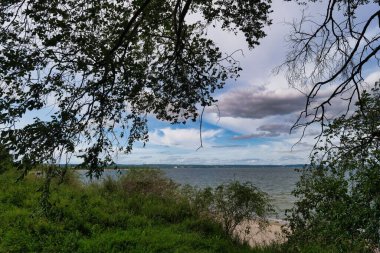 Bereketli yeşil ağaçlar parçalı bulutlu bir gökyüzünün altında sakin bir göl oluştururlar. Yumuşak dalgalar kıyıya vurur. Huzurlu bir atmosfer yaratır. Rahatlamak için mükemmel..