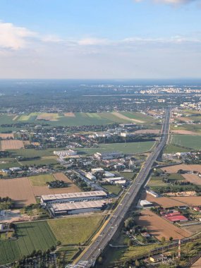 Havadan bakıldığında geniş alanlar ve kırsal araziyi kesen yoğun bir otoyol görülüyor. Parlak mavi bir gökyüzünün altında kentsel yapılar ve yeşil alanlar görülebilir..