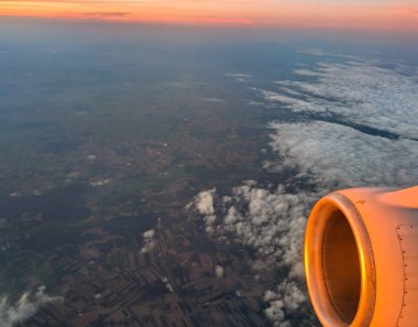 Gün batımının altın rengi bulutlar ve yeryüzü altında uzanırken uçak motorundan yansıyor. Sakin gökyüzü, akşam yolculuğu boyunca sakin bir atmosfer yaratır..