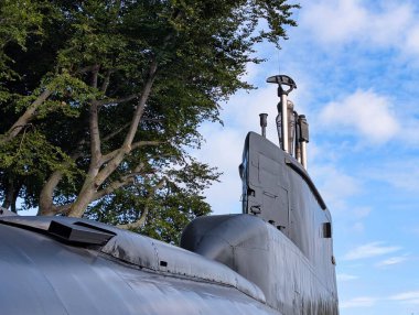 Açık bir gökyüzünün altında yemyeşil ağaçlardan oluşan bir zemin üzerinde bir denizaltı sergileniyor. Gemiler kule ve periskoplar açıkça görülüyor.,