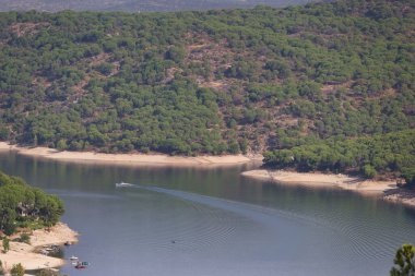 Huzurlu bir göl, kayıklar suda süzülürken berrak mavi gökyüzünü yansıtır. Ağaçlar kıyı boyunca uzanır, dinlenmek için mükemmel sakin bir atmosfer yaratır..