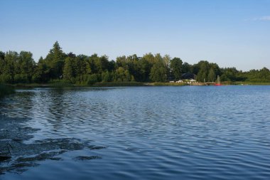 Sakin su, güneş dingin göl üzerinde batarken berrak gökyüzünü yansıtır. Bereketli ağaçlar kıyı şeridini çevreleyerek huzur verici bir rahatlama ortamı yaratıyor..