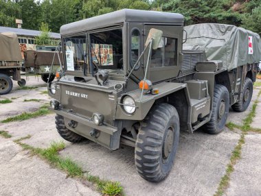 Bir askeri hizmet aracı, parlak gündüz vakti, tarihi bir yerde engebeli tasarımı ve klasik çekiciliğini sergileyerek önemli bir askeri sergide duruyor..