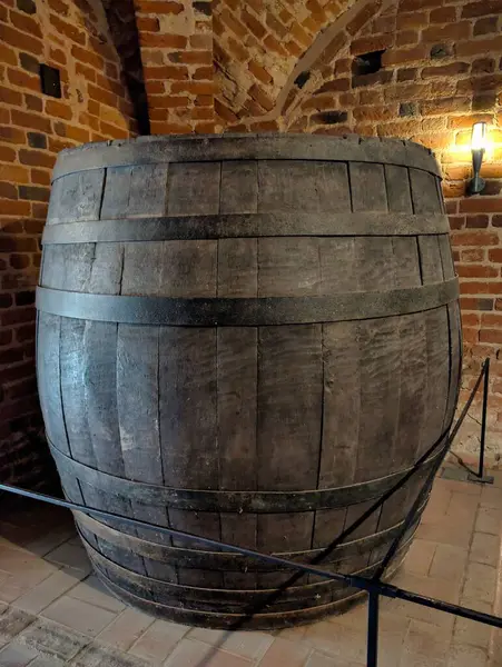 Geleneksel işçiliğin göstergesi olarak tuğla bir mahzende belirgin bir ahşap fıçı duruyor. Koyu renk ahşap, taş duvarlarla çelişiyor. Tarihi ve depolama tekniklerini koruyor..