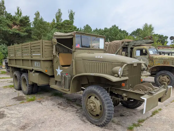 Yıldız işareti ile zeytin yeşiline boyanmış eski bir askeri kamyon arka planda ağaçlarla çakıllı bir yüzeye park edilmiştir. Araç klasik tasarımı ve sağlam yapısını sergiliyor..