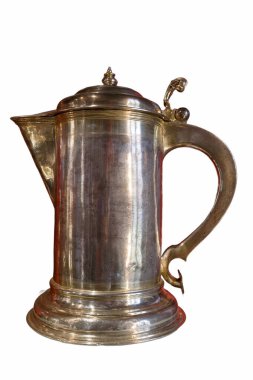 Detaylı bir gümüş sürahi, parlak yüzeyi ve zarif sapıyla dimdik ayakta duruyor. Güneş ışığı parlatılmış metalden yansıyarak işçiliğini ve şeklini vurgular..