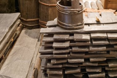 Wooden boards are neatly stacked atop one another in a rustic workshop. Nearby, aged barrels add to the vintage charm, reflecting traditional craftsmanship. Natural lighting enhances the textures.