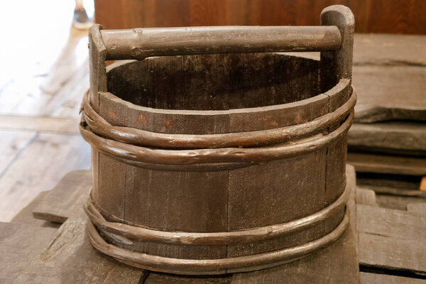 A wooden bucket made of dark wood sits atop a weathered surface. The bucket has a sturdy handle and metal bands, reflecting traditional craftsmanship in a rustic setting.