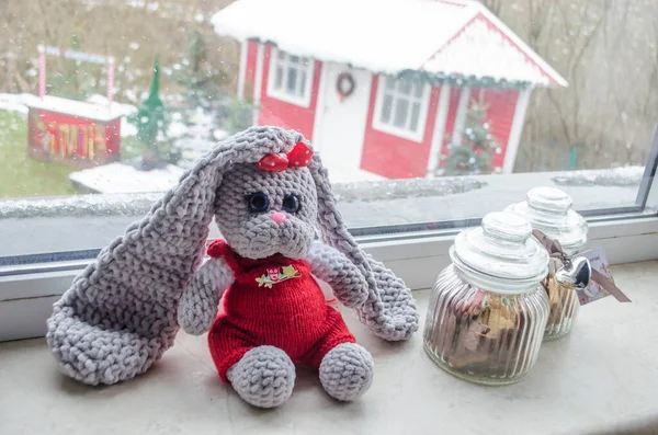 Knitted New Year\'s hare toy on the background of a Christmas house. Handmade toy.