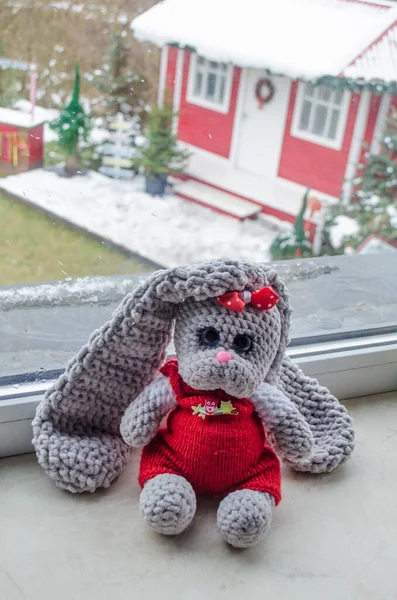 Knitted New Year\'s hare toy on the background of a Christmas house. Handmade toy.
