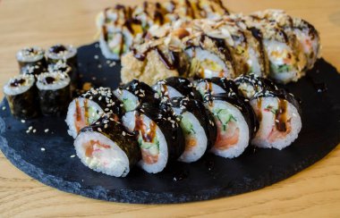 Suşi ve rulo, Asya mutfağı siyah tahta tabakta farklı türde. Lezzetli yemek fotoğrafı.