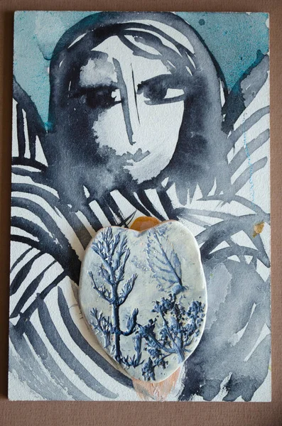 Watercolor and acrylic painting angel with ceramic blue heart with plant texture. Handmade photo.