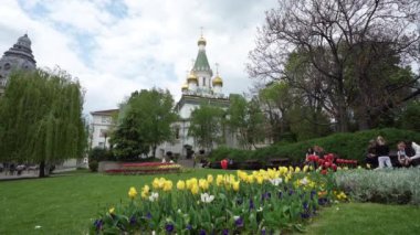 Sofya, Bulgaristan. Mayıs 2023 'te şehir merkezindeki bir parkta, arka planda Aziz Nicholas Kilisesi' nin kubbeleri olan renkli laleler.