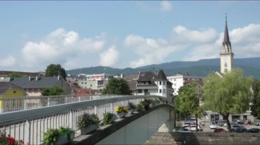 Villach, Avusturya. 18 Temmuz 2023 Drava nehri üzerindeki bir köprüden şehrin panoramik manzarası.