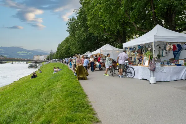 Salzburg, Avusturya. 1 Temmuz 2024 Pazar pazarının şehir merkezindeki Salzach nehrinin kıyısındaki tezgahlarının manzarası.