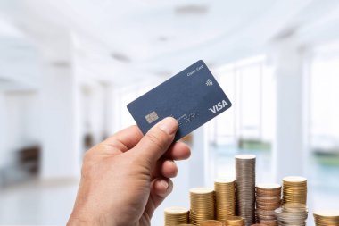 Italy, june 22, 2025. VISA brand credit card in in the hand with a some piles of coins  in the background