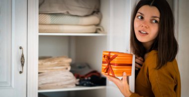 A funny young girl is in a hurry to hide a gift for a loved one, husband, children, friends and parents, a woman wants to make a surprise and hides the gift in the closet during holidays.
