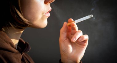 Genç bir güzel kız sigara içiyor, bir kadın stresli ve elinde bir sigara tutuyor, evinin penceresinin yanında duruyor, yakın çekim manzarası var..