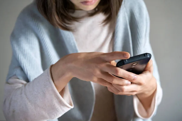 A young well-groomed woman holds a smartphone in her hands, communicates with colleagues, friends, a girl in a casual sweater works online using her mobile device.