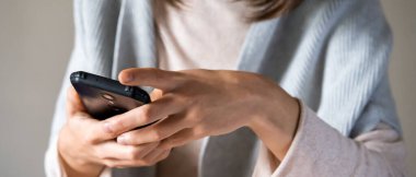 İyi giyimli genç bir kadın elinde bir akıllı telefon tutuyor, iş arkadaşları, arkadaşları, sıradan kazaklı bir kız cep telefonuyla internette çalışıyor..