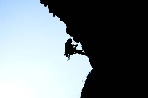 The black silhouette of a person climbs up the mountain against the background of the sky, leading an active lifestyle and involved in extreme sports, mountaineering and rock climbing.