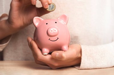 Womens hands carefully hold the piggy bank to preserve wealth, savings and financial success. A girl puts a coin in a piggy bank. clipart