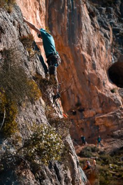 Genç bir adam ekstrem sporlarla meşgul, aktif bir hayat sürüyor, güneşli bir günde tırmanma ekipmanlarıyla bir kayaya tırmanıyor ve arka planda İkiz Mağaralar, Leonidio, Arcadia, Yunanistan.