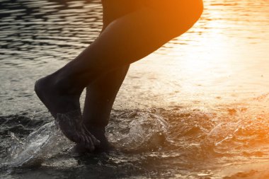 Suyun üzerinde sahil boyunca koşan biri, güneş ışınlarında okyanus ya da deniz, sporcu, antrenman yapıyor, dışarıda koşuyor, bacaklara yakından bakıyor ve su sıçratıyor..