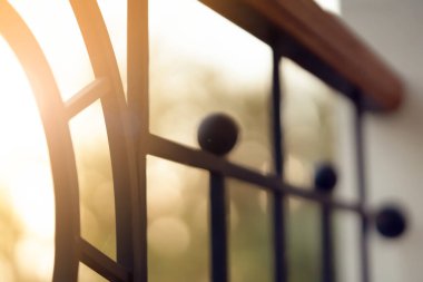 Zarif dekorlu dövülmüş şık kapılar, güneşli bir akşamın arka planında kıvrımlı çizgileri olan verandada bir çit, yakın çekim manzaralı..