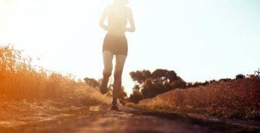 Genç spor kızı üstte ve şortlu dışarıda antrenman yapıyor, gün batımında koşuyor. Bir kadın uzun bir yarışa hazırlanmak için açık havada koşuyor, aktif bir yaşam tarzından hoşlanıyor..