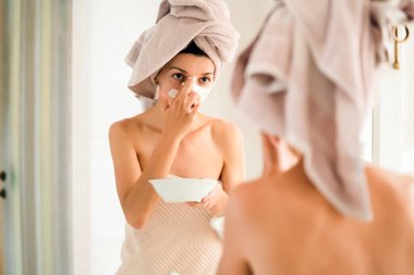 Kafasına ve vücuduna havlu geçirmiş genç bir kız banyoda aynanın yanında duruyor ve yüzüne kilden bir maske takıyor. Kadın sağlığına ve güzelliğine dikkat ediyor..