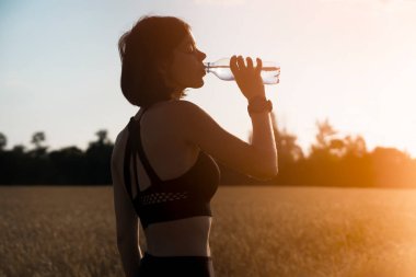 Genç bir kız yoğun bir idman sırasında mola verir ve koşar ve şişeden serin su içer. Bir kadın akşamüstü dışarıda idman yapar..