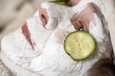 An elderly woman takes care of her health and beauty, applies a cosmetic mask on her face, has a good time, close-up view. clipart