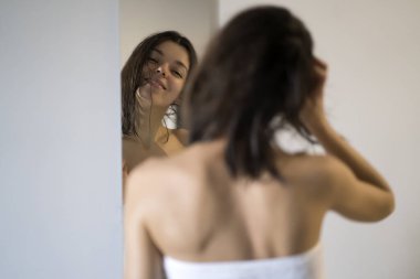 Duştan ve hijyenik prosedürlerden sonra, havluya sarılmış güzel bir kız aynada kendine bakar, saçına maske takar, evde cilt bakımı yapar..